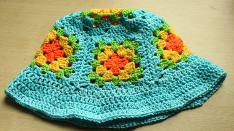May include: A crocheted sun hat with a blue base and colorful squares featuring yellow, orange, and green accents.
