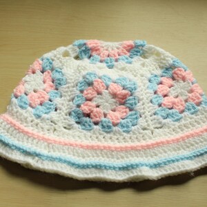 May include: White crochet sun hat with pink and blue squares. The hat has a wide brim and is made of a soft, lightweight yarn.