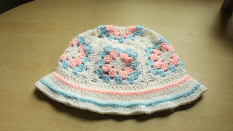 May include: White crochet sun hat with pink and blue squares. The hat has a wide brim and is made of a soft, lightweight yarn.
