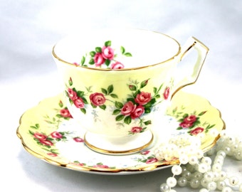 Könnte beinhalten: Eine gelbe Teetasse und Untertasse mit einem Blumenmuster aus rosa Rosen und grünen Blättern. Tasse und Untertasse haben einen goldenen Rand.
