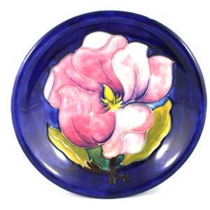Puede incluir: Un plato de cerámica azul con un diseño de flor de magnolia rosa y blanca. La flor está en el centro del plato y tiene hojas verdes.
