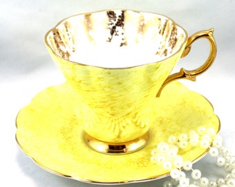 May include: A yellow teacup and saucer set with gold trim. The cup and saucer feature a delicate floral pattern. A string of pearls is in the foreground.