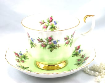 May include: A green and white teacup and saucer set with a floral pattern. The cup and saucer have a gold trim.