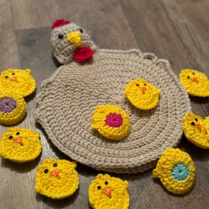 May include: A crocheted chicken with yellow chicks. The chicken is beige with a red comb and beak. The chicks are yellow with black eyes and orange beaks. There are also some crocheted eggs in different colors.
