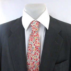 May include: A dark gray suit jacket with a white dress shirt and a floral tie. The tie features a pattern of small red, yellow, and blue flowers on a white background. The suit is displayed on a mannequin.
