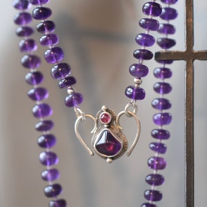 Puede incluir: Un collar de piedras preciosas de amatista púrpura con un cierre de plata y un colgante con una piedra de amatista más grande y una piedra rosa más pequeña.