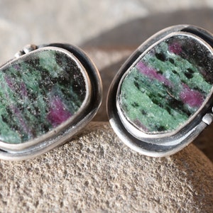 May include: A pair of silver earrings with green and pink gemstone cabochons set in a bezel setting.