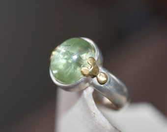 May include: A silver ring with a green gemstone and gold accents.