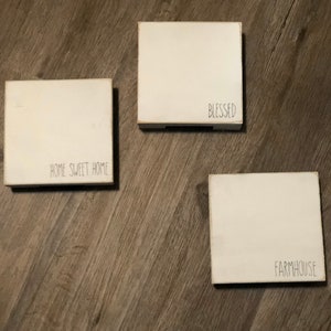 May include: Three white wooden signs with black lettering. The signs read "Home Sweet Home", "Blessed", and "Farmhouse".