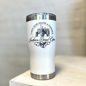 May include: White stainless steel tumbler with a black and white graphic of a tractor and the text "Then God Made a Farmer Southern Drawl Cotton".
