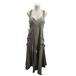 May include: Olive green dress with a V-neckline and wide straps. The bodice is embellished with silver sequins and beads. Ruffles adorn the skirt and the dress has a flowing, asymmetrical hemline. The dress is displayed on a mannequin.