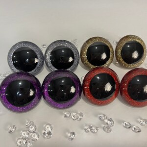 Puede incluir: Seis pares de ojos de pl&aacute;stico con detalles de purpurina. Los ojos son negros con un borde de purpurina plateado, morado, dorado o rojo.