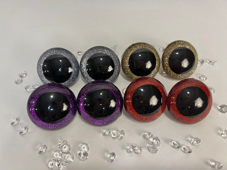 Puede incluir: Seis pares de ojos de pl&aacute;stico con detalles de purpurina. Los ojos son negros con un borde de purpurina plateado, morado, dorado o rojo.