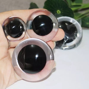 Puede incluir: Cuatro ojos saltones de pl&aacute;stico de diferentes tama&ntilde;os. Los ojos son transparentes con pupilas negras. Los ojos est&aacute;n en una mano.
