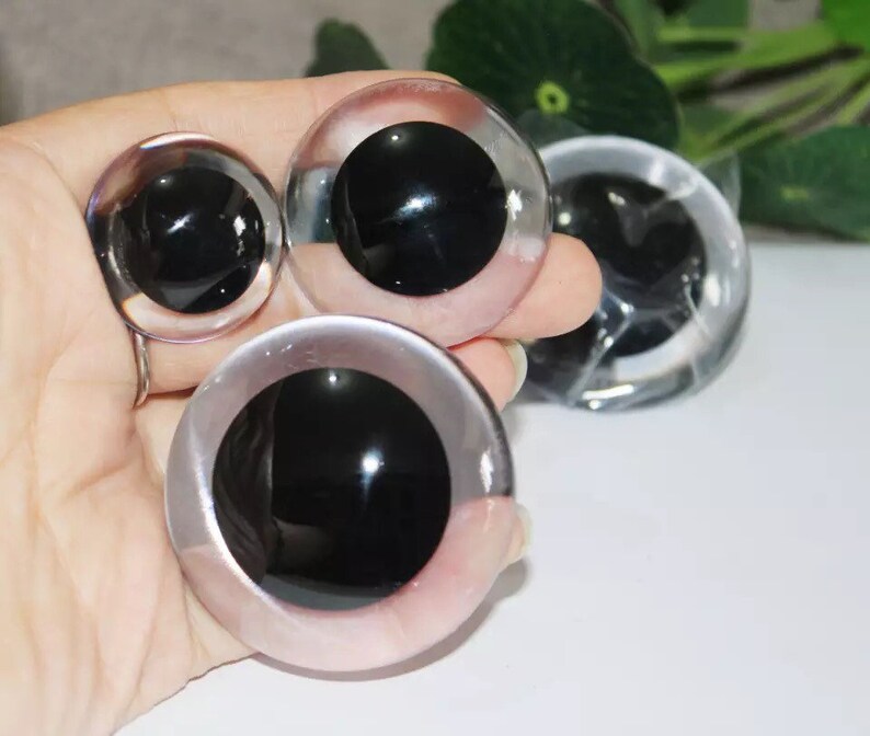 Puede incluir: Cuatro ojos saltones de pl&aacute;stico de diferentes tama&ntilde;os. Los ojos son transparentes con pupilas negras. Los ojos est&aacute;n en una mano.