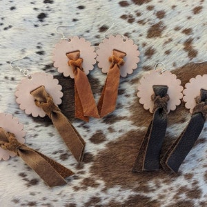 Peut inclure: Trois paires de boucles d'oreilles en cuir avec un pendentif en cuir tressé. Les boucles d'oreilles sont en cuir marron, beige et noir. Les boucles d'oreilles ont la forme d'un cercle avec un bord festonné.