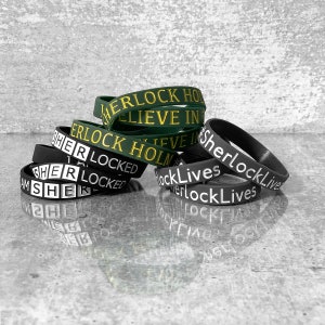 Op de afbeelding: Een stapel zwarte en groene siliconen polsbandjes met de tekst "Sherlock Lives" en "Sherlock Holmes" erop gedrukt.