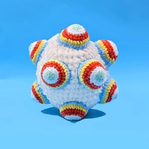 May include: A white crocheted ball with colorful stripes. The ball has six points, each with a circle of red, yellow, blue, and green yarn.