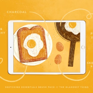 May include: A digital illustration of a tablet screen showing a breakfast scene with a fried egg on toast, a frying pan with a fried egg, and three eggs on a yellow background. The text "SKETCHING ESSENTIALS BRUSH PACK // THE GLADDEST THING" is at the bottom of the screen. The tablet is surrounded by a yellow background with handwritten text describing different brush styles: "SOFT & SCRATCHY", "CHARCOAL", "PAPER TIGER", and "SKETCHING PENCIL".