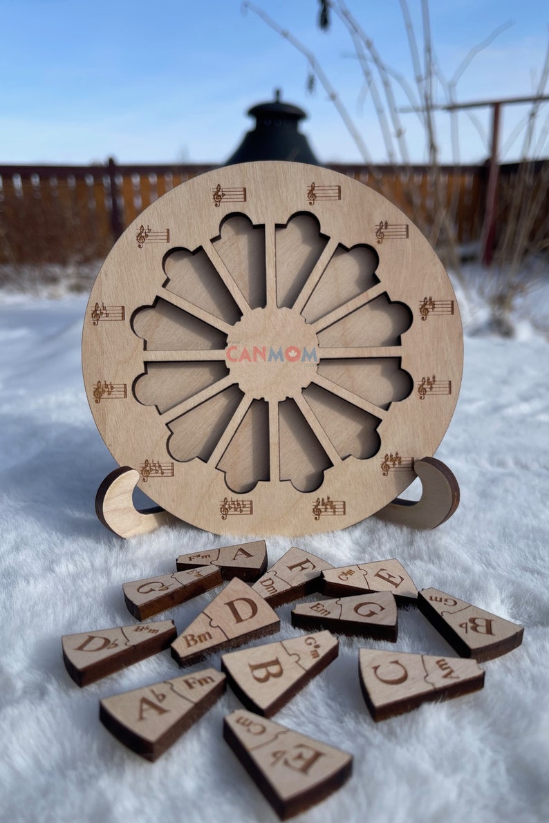 Puede incluir: Un c&iacute;rculo de madera con un dise&ntilde;o de nota musical y 12 ranuras alrededor del borde. Hay 12 piezas de madera con notas musicales y letras en ellas. Las piezas est&aacute;n esparcidas sobre una superficie blanca.