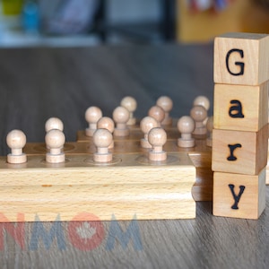 Könnte beinhalten: Holzböcke, die den Namen "Gary" buchstabieren, mit einem Satz hölzerner Knöpfe im Hintergrund.