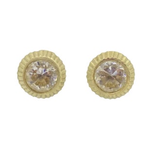 May include: A pair of gold earrings with a round, clear stone set in a textured, gold setting.