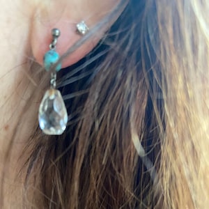 May include: A pair of silver dangle earrings with a turquoise bead and a clear crystal teardrop pendant.