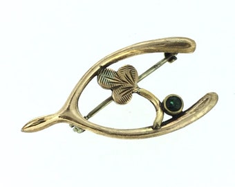 May include: Gold-toned horseshoe-shaped brooch with a green gemstone and a clover design.