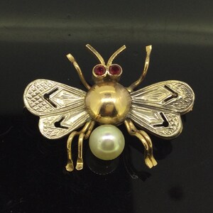 May include: A gold bee brooch with red gemstone eyes and a pearl accent.