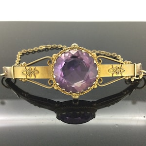 Könnte beinhalten: Ein goldenes Armband mit einem großen, runden, violetten Amethyst-Edelstein, der in einem filigranen Design gefasst ist.