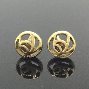 May include: A pair of gold-toned earrings with a circular design featuring a stylized floral pattern.