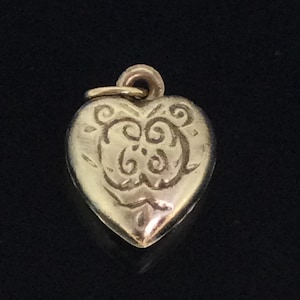 Puede incluir: Un amuleto de corazón de oro con un diseño decorativo de espiral.