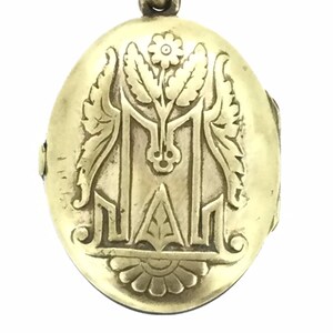 K&ouml;nnte beinhalten: Goldenes ovales Medaillon mit einem gravierten Blumendesign und einem Monogramm. Das Medaillon hat einen Klappdeckel und eine Schlaufe zum Anbringen einer Kette.