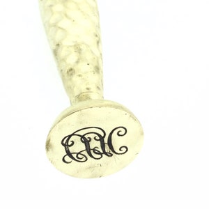 May include: A silver seal with a hammered handle and a round base. The base has the initials "C.C." engraved in a cursive font.