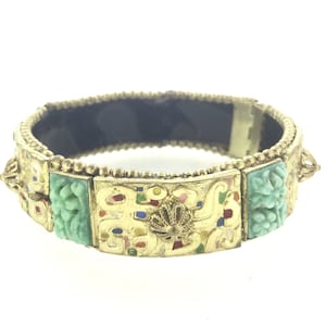 Könnte beinhalten: Ein goldfarbenes Armband mit grünen und mehrfarbigen Emaille-Akzenten. Das Armband hat ein dekoratives Blumenmuster und ist aus Metall.