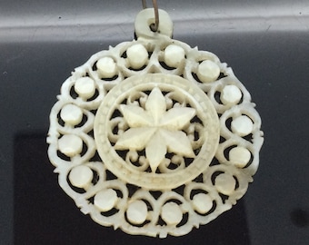 May include: A white carved pendant with a floral design. The pendant has a loop at the top for hanging.