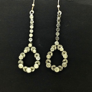 Może przedstawiać: Para srebrnych kolczyków wiszących w kształcie łzy z kółkiem z przezroczystych cyrkonii. Kolczyki mają złote zapięcie na haczyk.