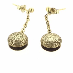 May include: A pair of gold dangle earrings with a floral design on the round pendant. The earrings have a chain connecting the pendant to the post.
