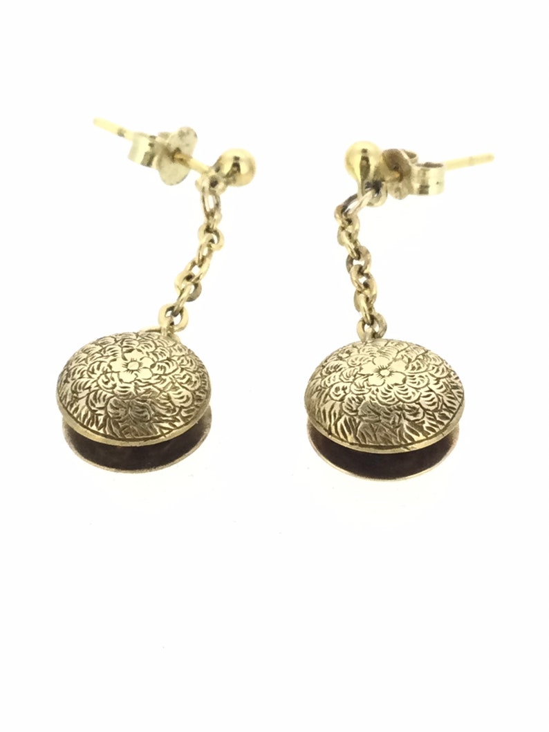 May include: A pair of gold dangle earrings with a floral design on the round pendant. The earrings have a chain connecting the pendant to the post.