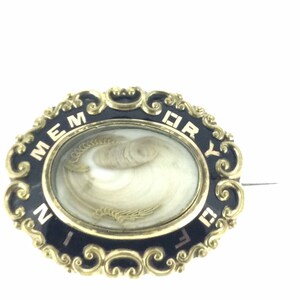 May include: A gold-toned oval locket with black enamel and gold lettering that reads "IN MEMORY OF". The locket contains a lock of hair.