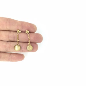 May include: A pair of gold dangle earrings with small round discs at the end of the chains.