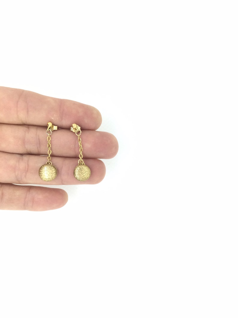 May include: A pair of gold dangle earrings with small round discs at the end of the chains.
