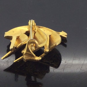 May include: A gold-toned brooch with a crescent moon design. The brooch is made of metal and has a pin back.