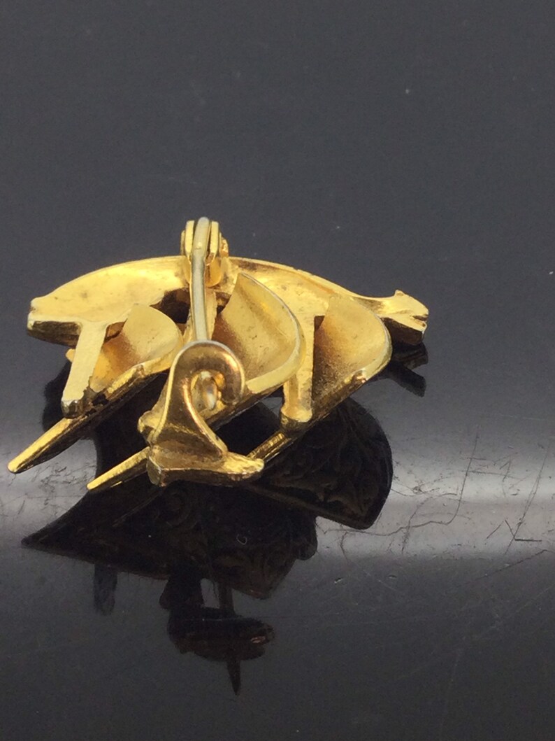 May include: A gold-toned brooch with a crescent moon design. The brooch is made of metal and has a pin back.