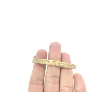 K&ouml;nnte beinhalten: Ein goldenes Armreif-Armband mit einem komplizierten Blumenmuster.
