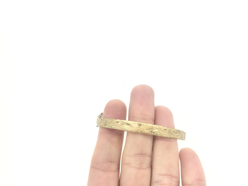 K&ouml;nnte beinhalten: Ein goldenes Armreif-Armband mit einem komplizierten Blumenmuster.