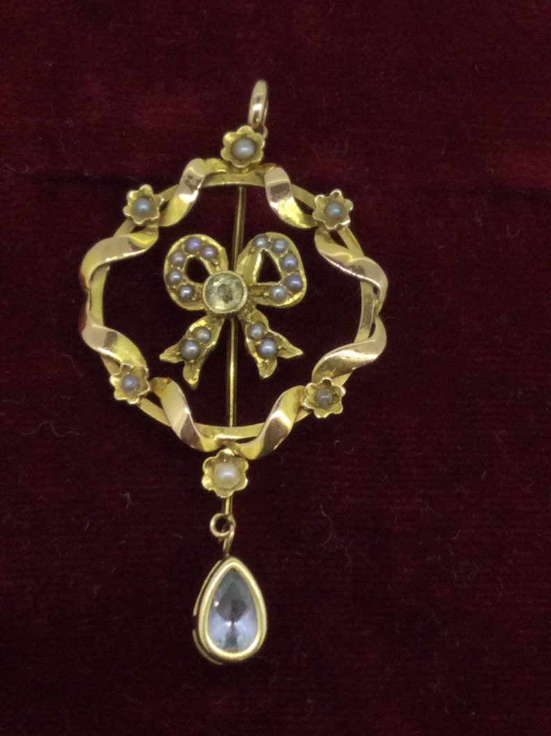 May include: A gold pendant with a pearl-encrusted bow and a teardrop-shaped blue stone hanging from the bottom.