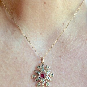 May include: A gold necklace with a star-shaped pendant. The pendant is adorned with small white pearls and a red gemstone in the center.