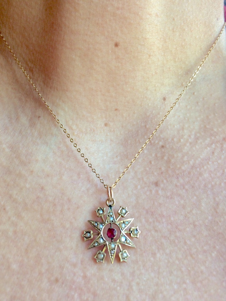 May include: A gold necklace with a star-shaped pendant. The pendant is adorned with small white pearls and a red gemstone in the center.