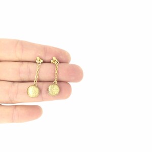May include: A pair of gold dangle earrings with small round discs at the end of the chains.